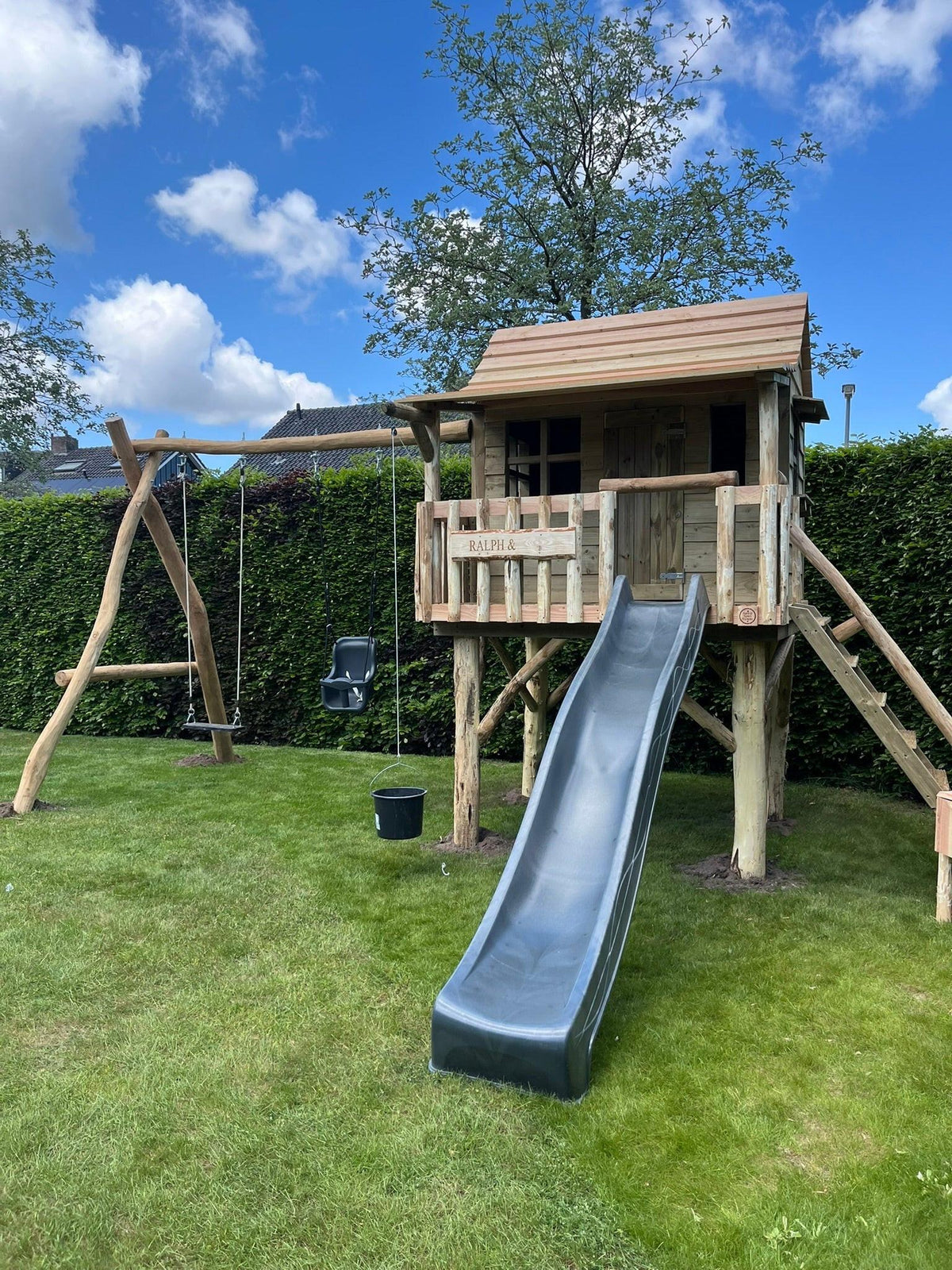 Houten speelhuisje De Berk met glijbaan in een kleine tuin